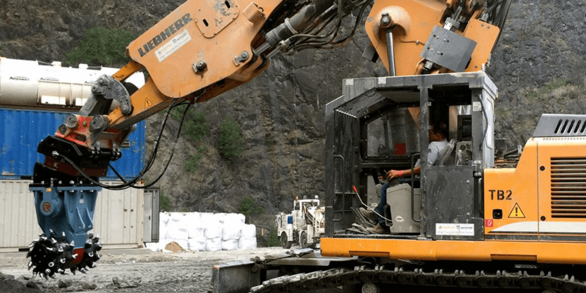 An excavator equipped with a rockwheel attachment grinds through rock